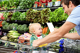 Adult shopping with child in cart choosing produce in supermarket